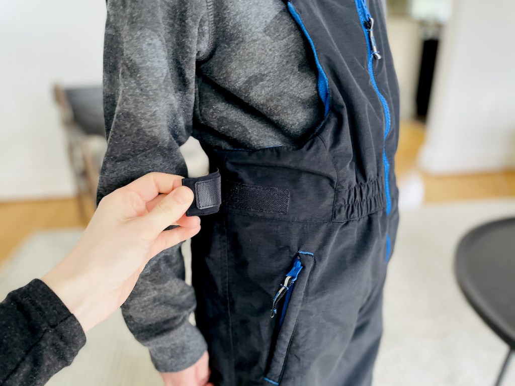 hand pulling off velcro strap from black pair of kids snow pants