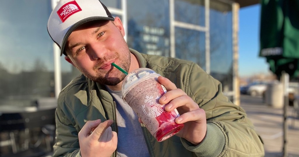 man holding a starbucks love bug drink taking sip from green straw
