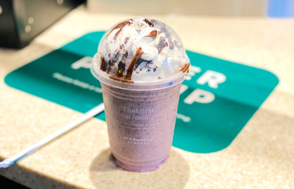 pink starbucks frappuccino with whipped cream and chocolate on starbucks countertop