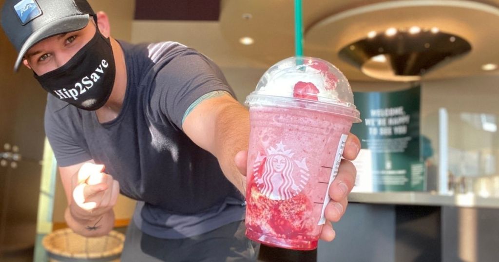 man holding up and pointing to a pink starbucks frappuccino