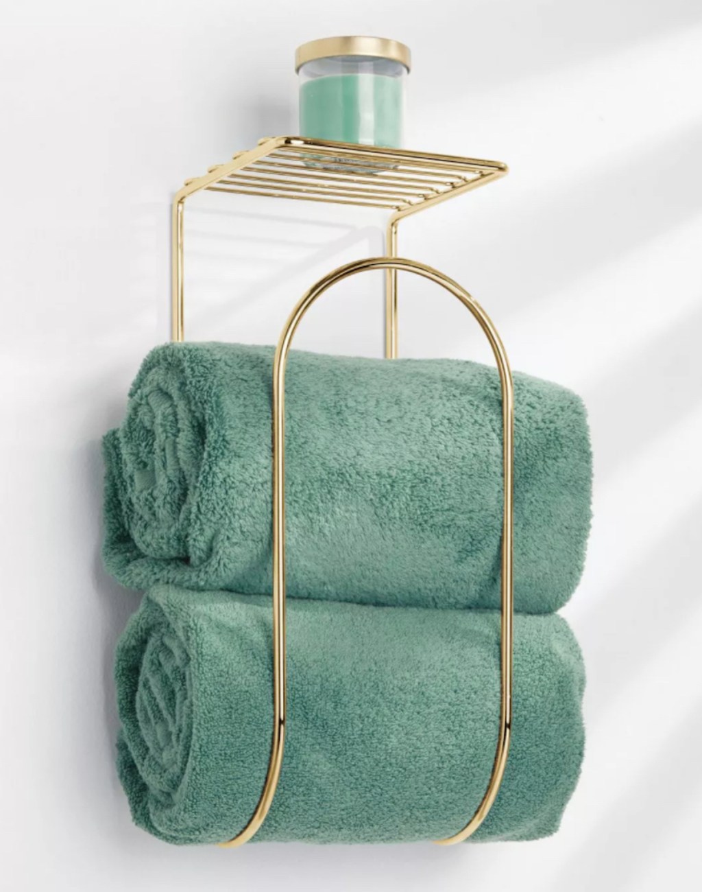 gold metal towel rack with teal towels and candle on shelf hanging on wall