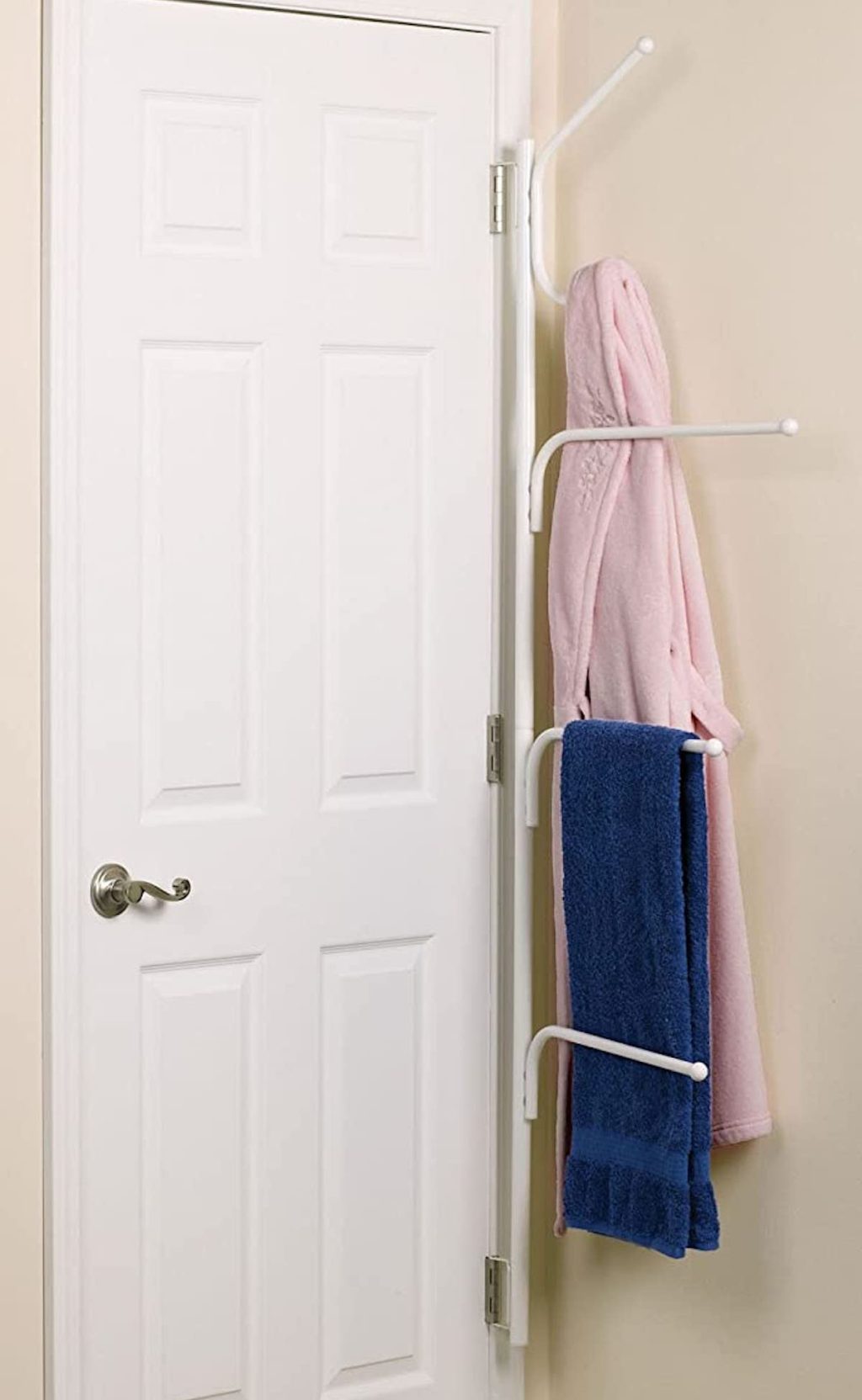 white metal towel rack hanging on back of door hinges in bathroom