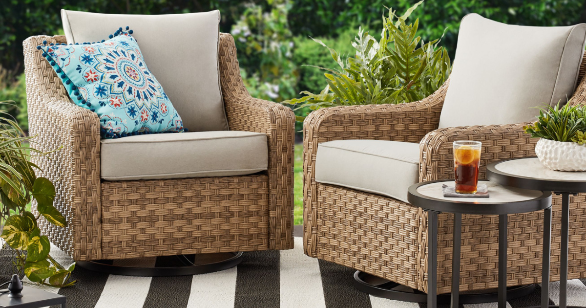 Two wicker swivel chairs outside with nesting tables next to them.