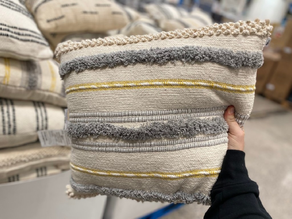 hand holding yellow and gray striped woven pillow in store