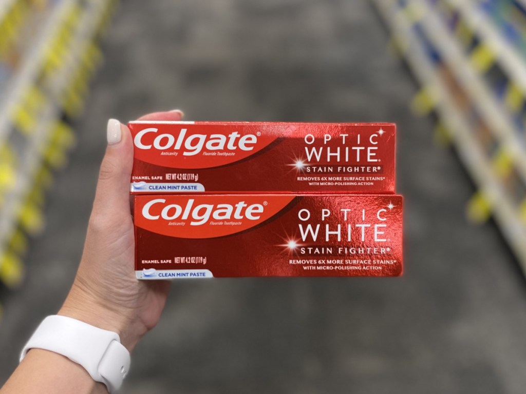 woman's hand holding 2 boxes of colgate toothpaste at cvs