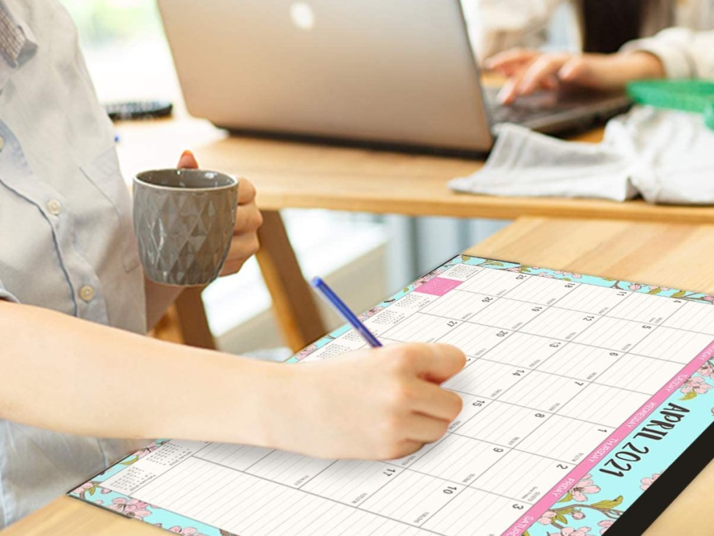 woman holding cup of coffee and writing on large desk calendar