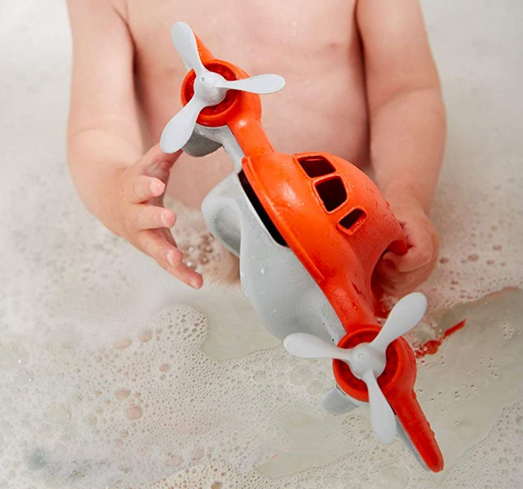 baby playing with red plane toy in bath tub