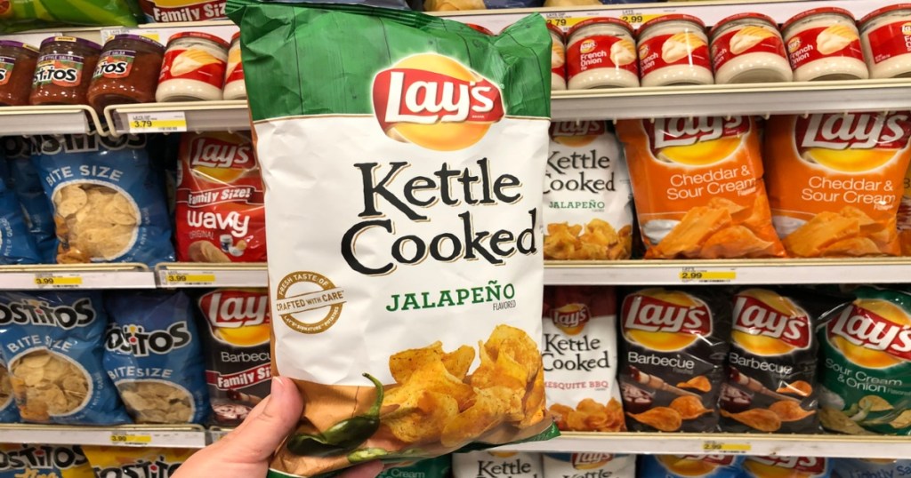 a hand holding a bag of Lay's Kettle cooked chips in store, in front of all bagged stocked chips in store