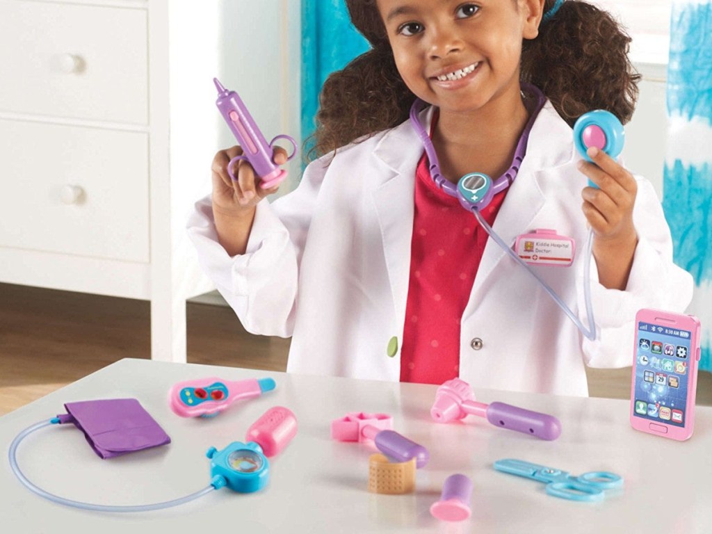girl in doctor's coat playing with pink doctor kit
