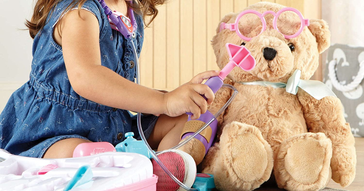 young girl dressed like a doctor using toys to give a teddy bear a checkup