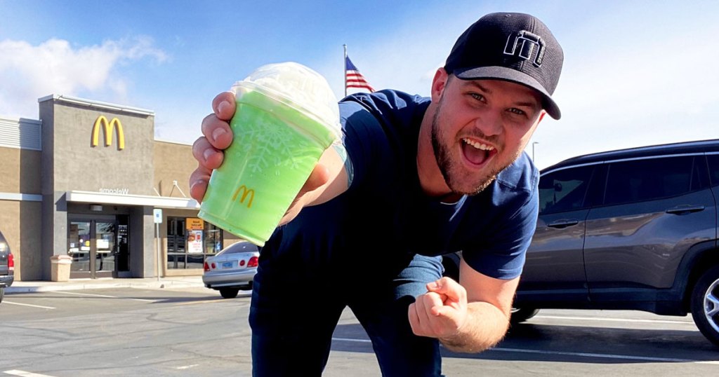 man holding and pointing at a green shamrock shake in front of mcdonalds