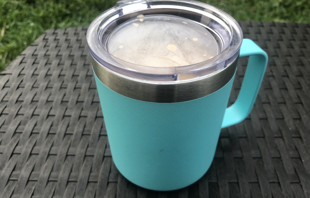 teal blue coffee mug with clear lid sitting on outdoor furniture