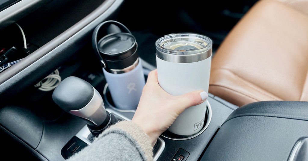 hand holding white yeti coffee tumbler in car cup holder