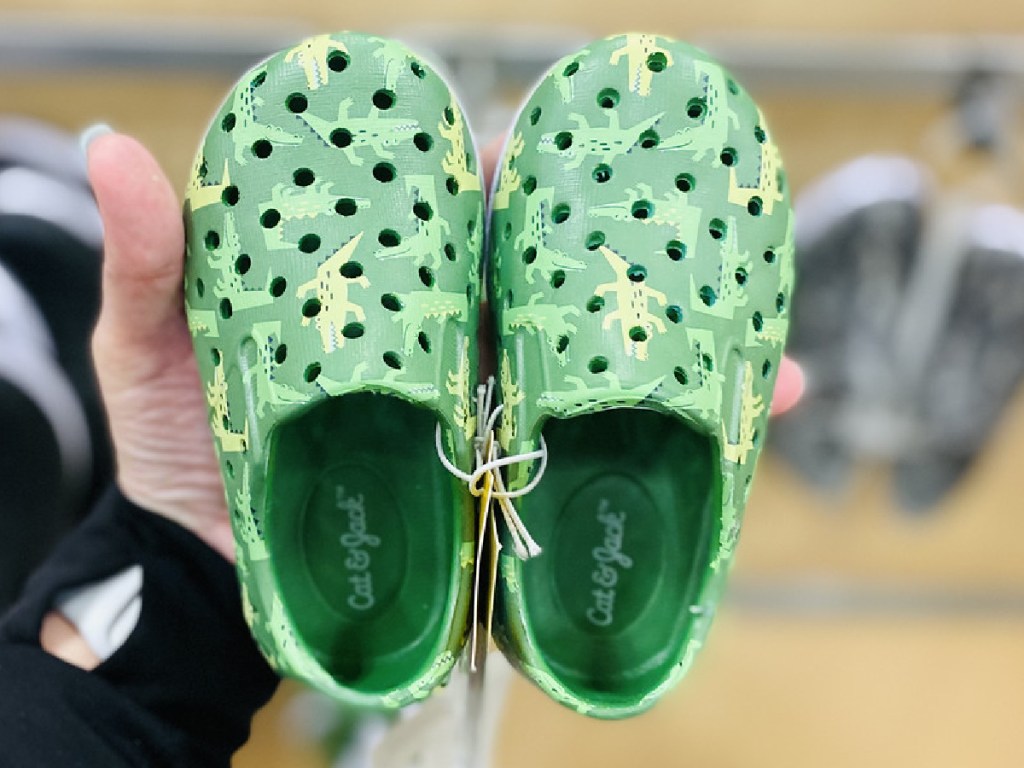 hand holding pair of kids green shoes with alligators on them