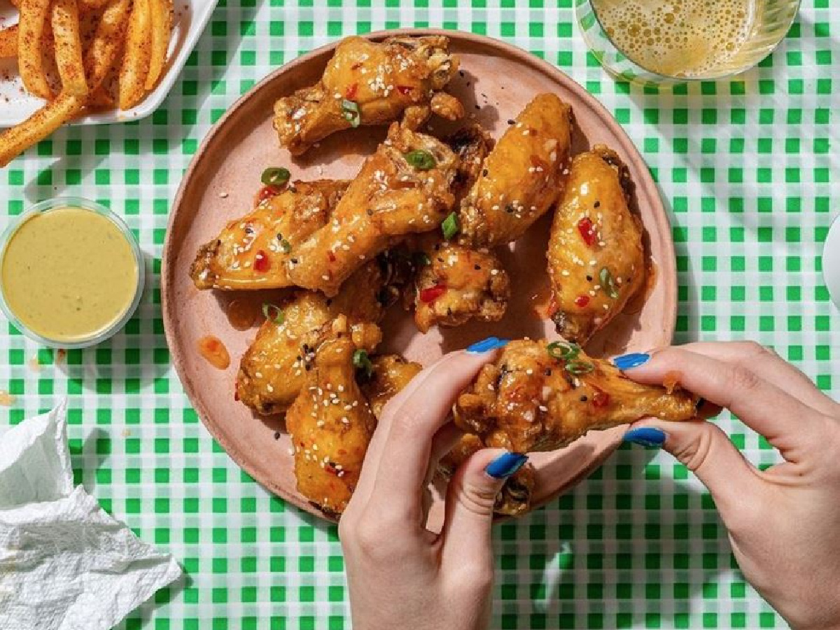 manicured hands holding chicken wings at table