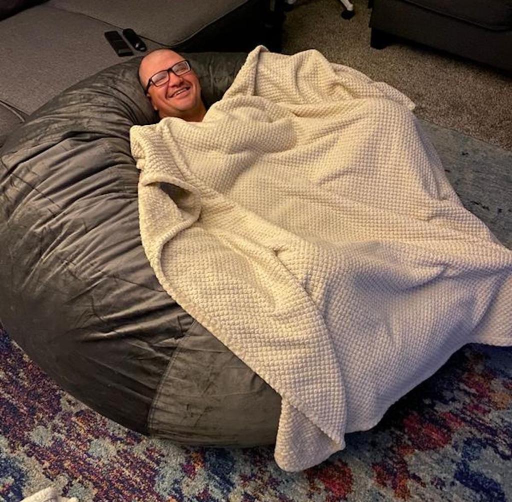 man laying on lovesac bean bag chair dupe with throw blanket
