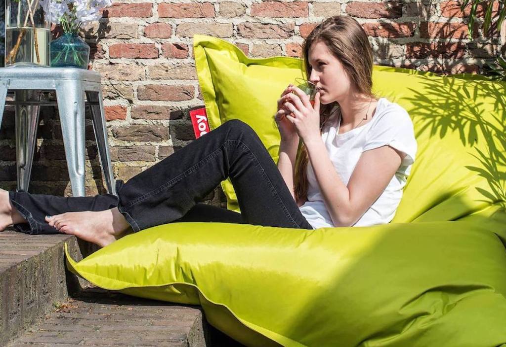 woman sipping drink while sitting outside on green square bean bag