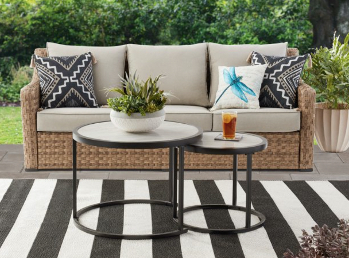 wicker patio sofa and two nesting tables on white and black stripe rug outside
