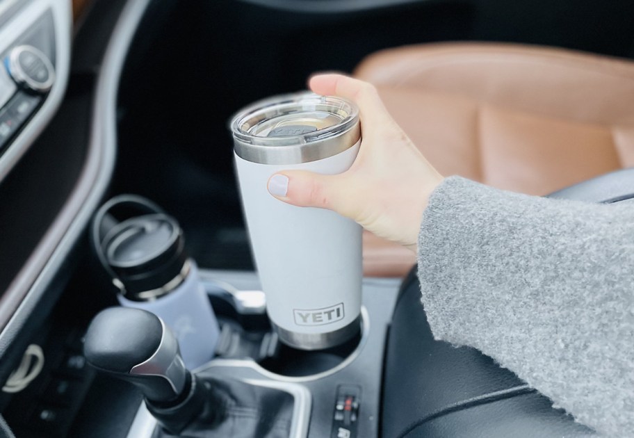 hand holding a white yeti coffee tumbler in car 