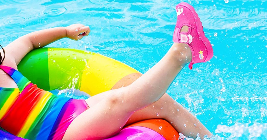 girl in rainbow bathing suit in pool with pink water shoes