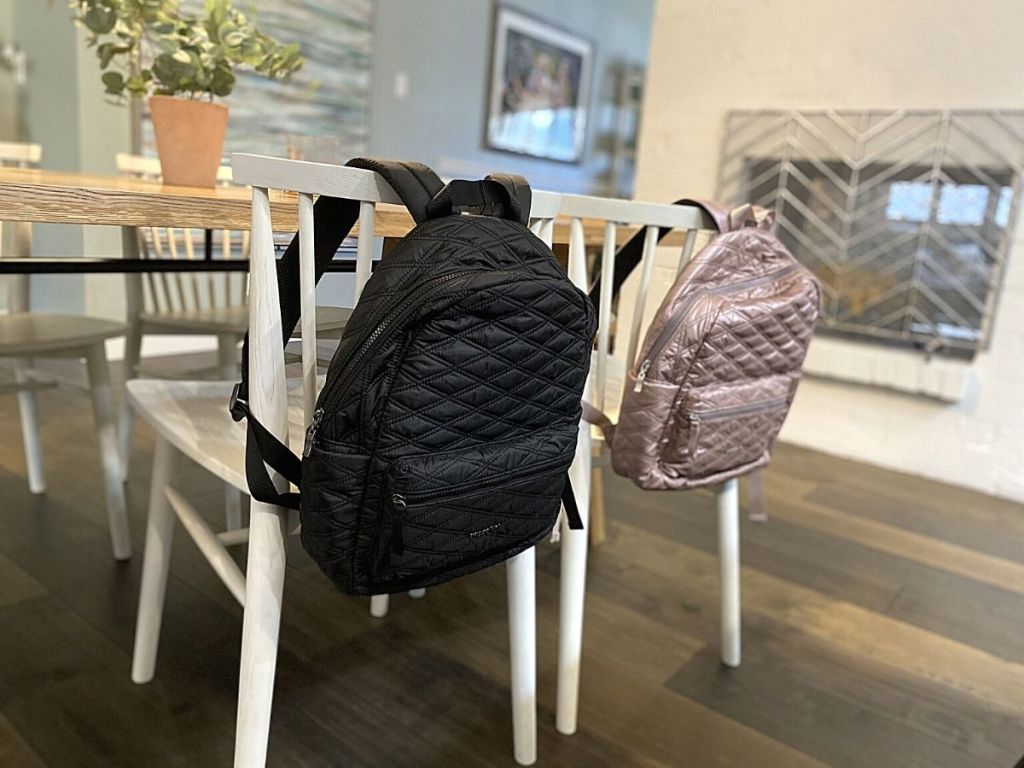 black and rose gold Baggallini backpacks hanging on white chairs