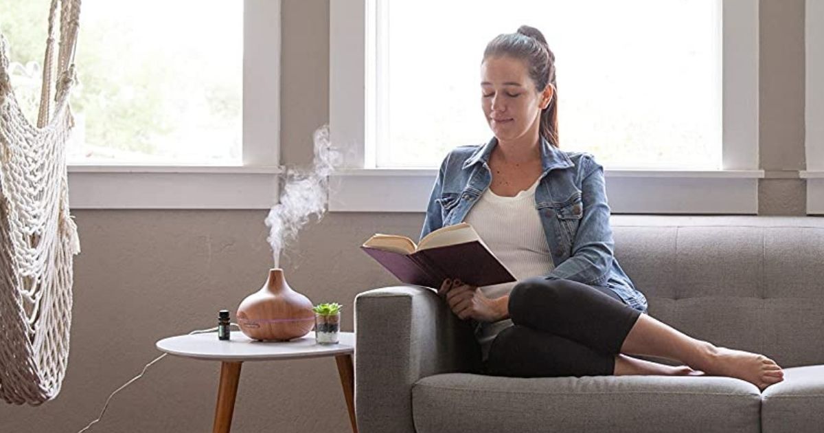 woman reading a book next to an essential oil diffuser