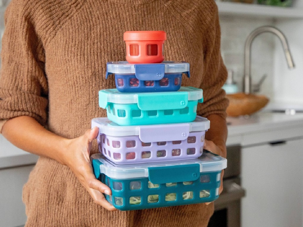 woman in kitchen holding five colored food storage containers