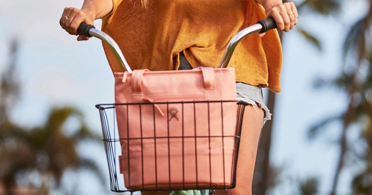 woman wearing an orange shirt riding a bike with a pink tote bag in the basket