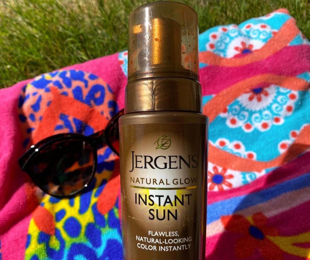 bottle of jergens self tanner, sunglasses, and beach towel