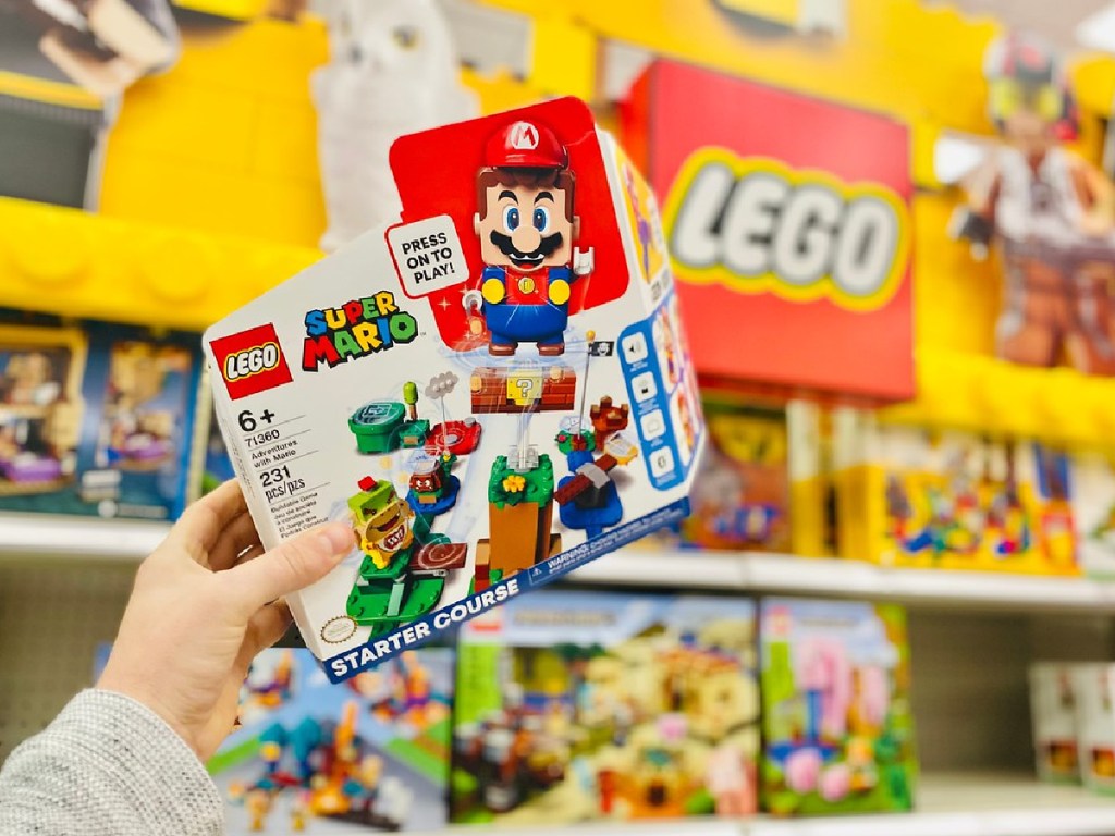 man's hand holding LEGO Super Mario kit in front of LEGO sign in store