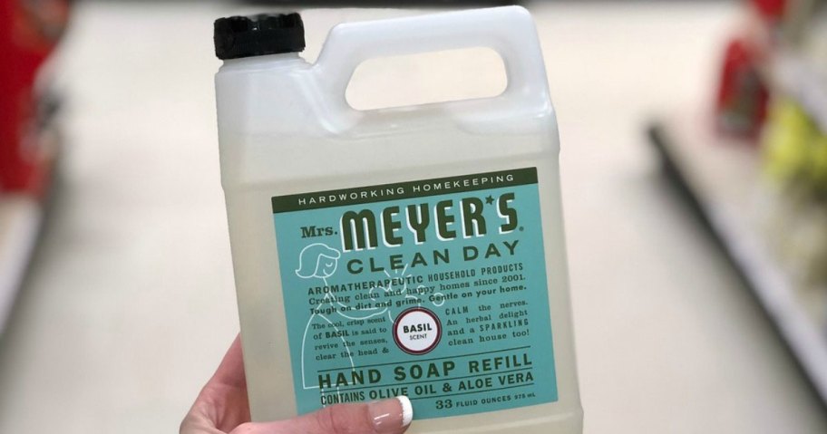 person holding up a mrs meyers hand soap refill bottle in basil scent