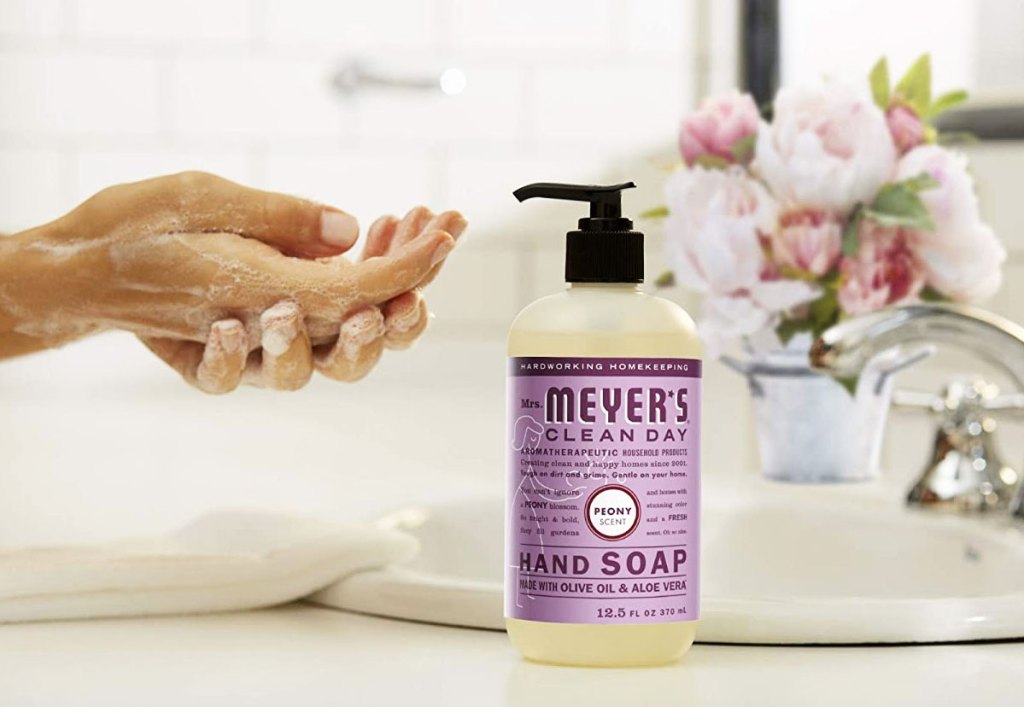 person washing hands next to a bottle of peony mrs meyers hand soap