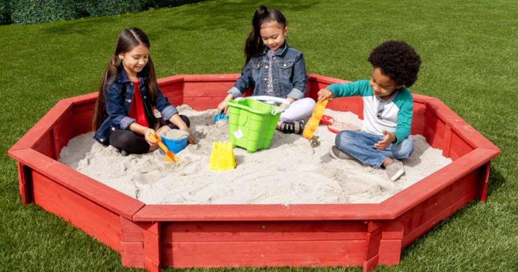 3 children sitting in a octagon sandbox outside