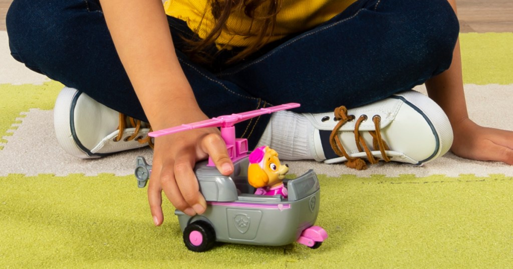 girl on floor playing with gray and pink helicopter toy with pup figure