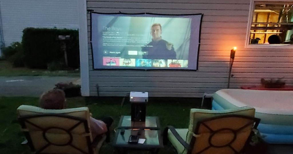 person sitting outside watching movie projected on side of house