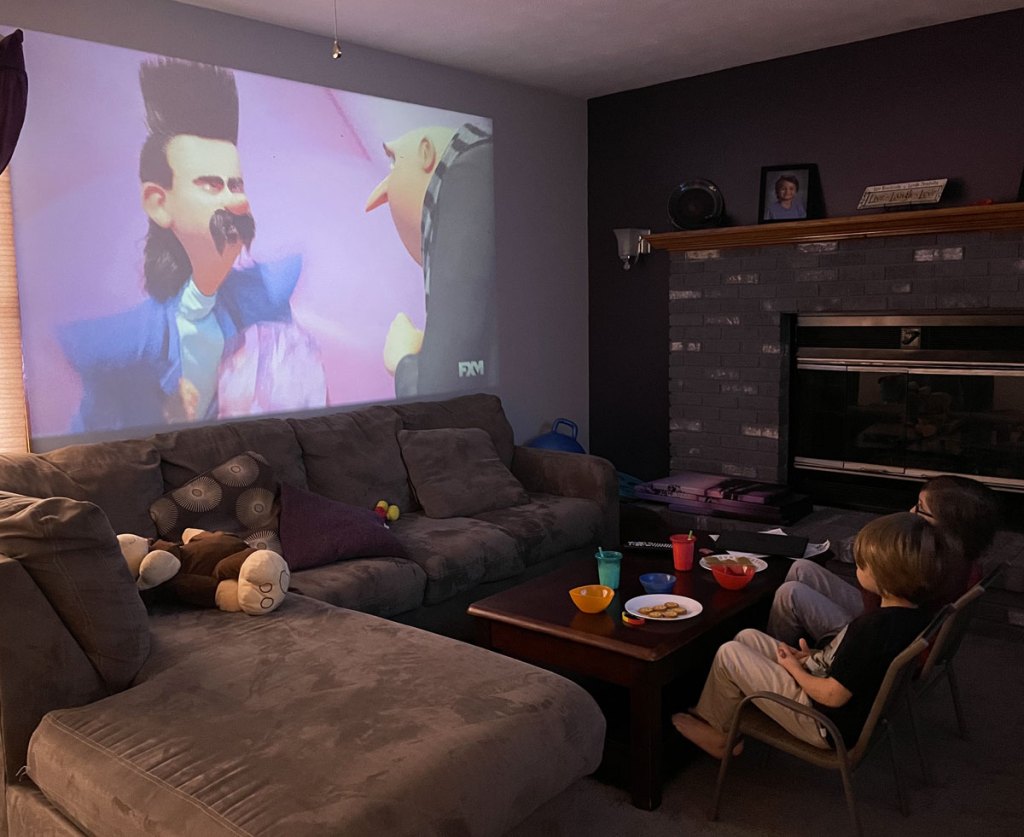 kids sitting in living room watching movie projected on wall