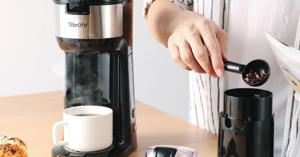 person adding coffee beans to grinder next to a coffee maker