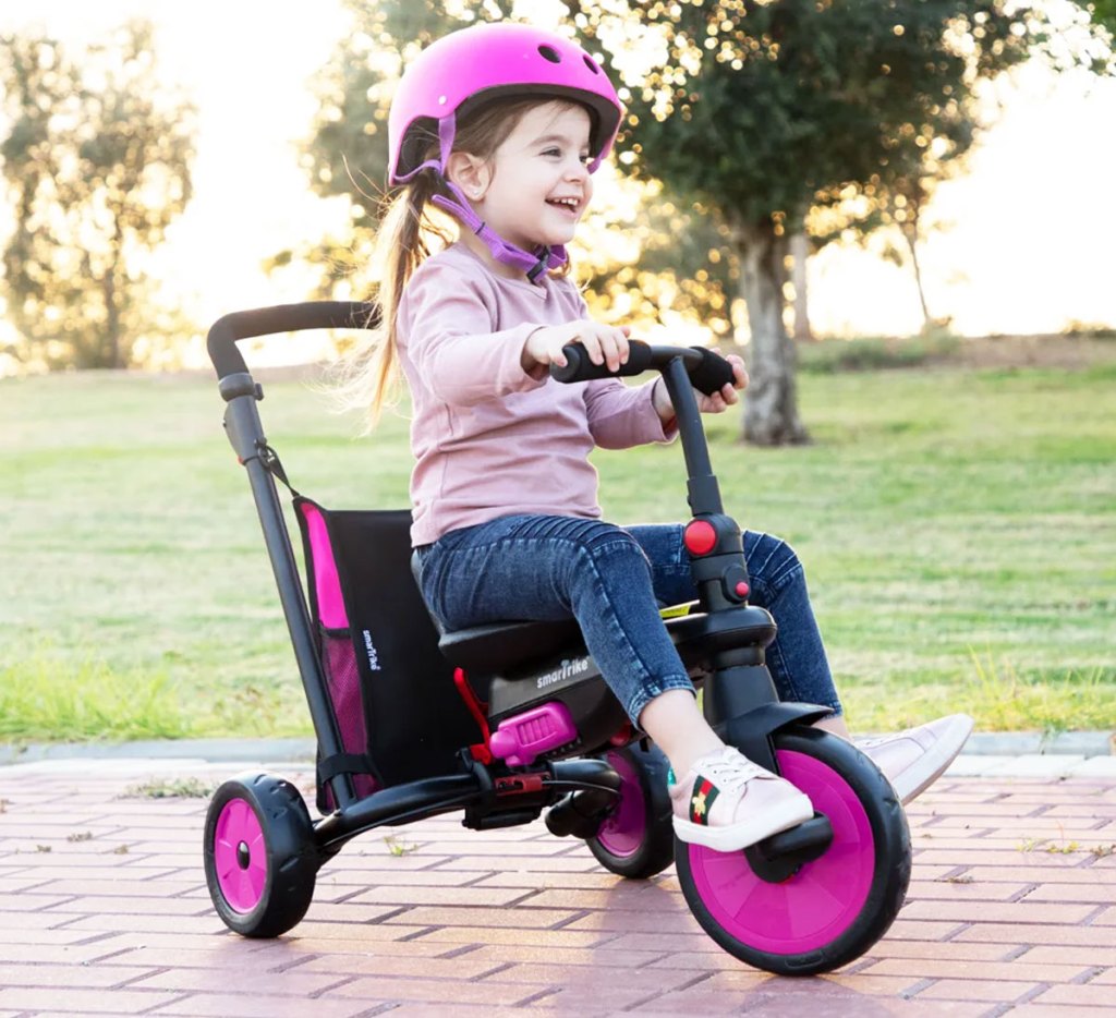 girl riding on a pink and black convertible tricycle