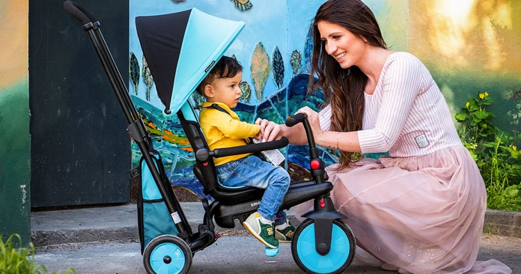 woman kneeling next to child in blue and black stroller trike