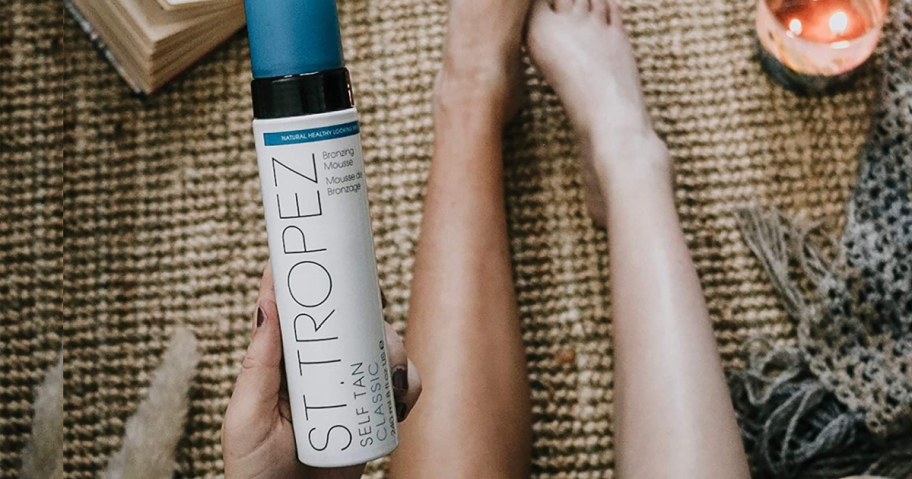 hand holding a St. Tropez Tanner next to 1 tanned leg and 1 untanned leg