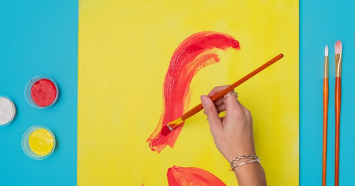 woman's hand holding a paintbrush doing abstract art on yellow paper