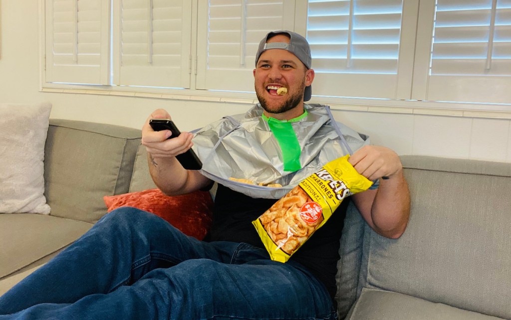 man holding bag of chips holding remote wearing an adult bib