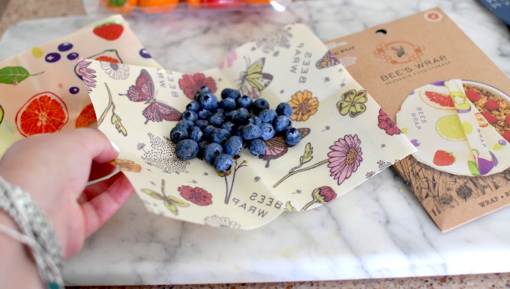 hand holding corner of bee's wraps reusable food wrap with blueberries