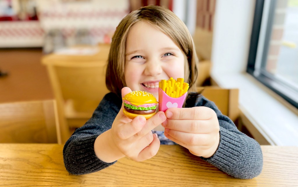 girl smiling holding miniature burger and fries lip balm