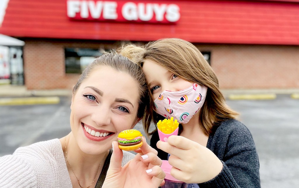 woman and girl standing outside of five guys holding mini burger and fries