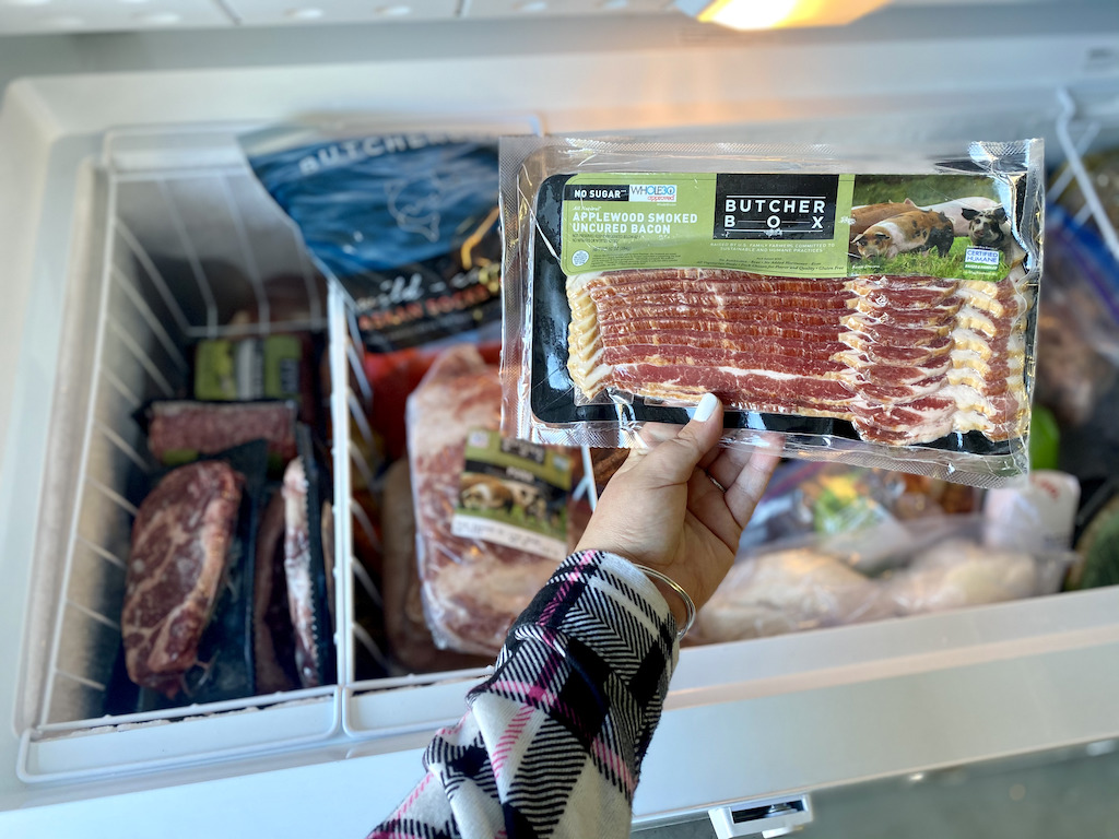 woman holding up Butcher Box frozen bacon with chest freezer in background