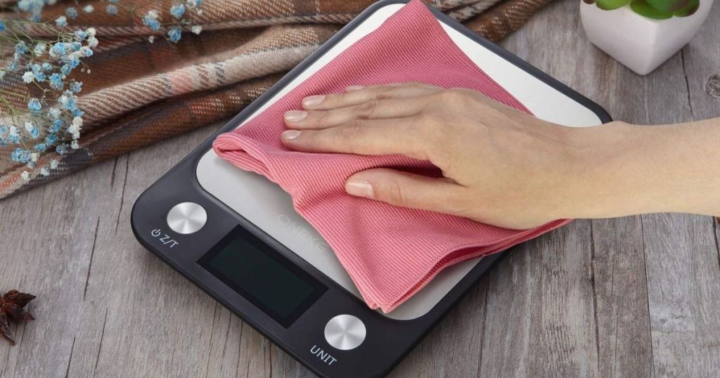hand wiping base of digital food scale with pink microfiber cloth