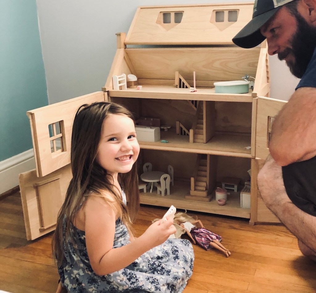 girl sitting in front of large wooden dollhouse