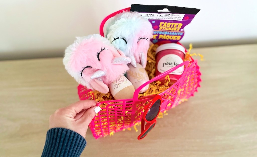 hand holding a pink easter basket with various easter goodies inside