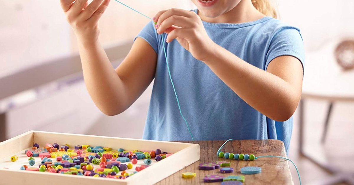 young girl at a table playing with a set of beads. Putting beads on a string.